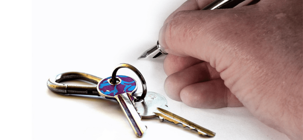 house keys and a man's hand about to sign something with a calligraphy pen - perhaps a rental agreement to relocate for a special needs child