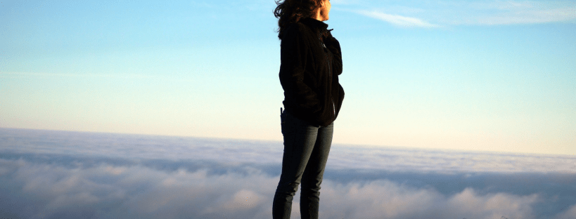 Confident strong woman (A special needs mum?), standing at the top of a hill, silhouetted against only clouds below and sky above.