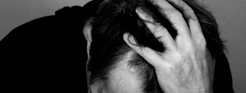 Man in dark clothing hunched over holding his head - sleep tips to cope with your child in hospital