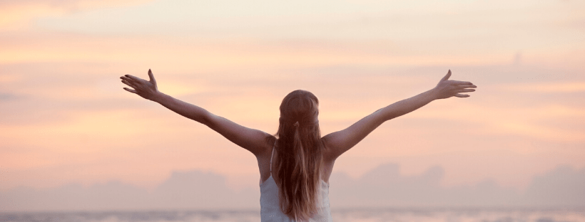 Woman arms out stretched - the sun just disappeared below the horizon at the beach - enjoying the benefits of healthy living